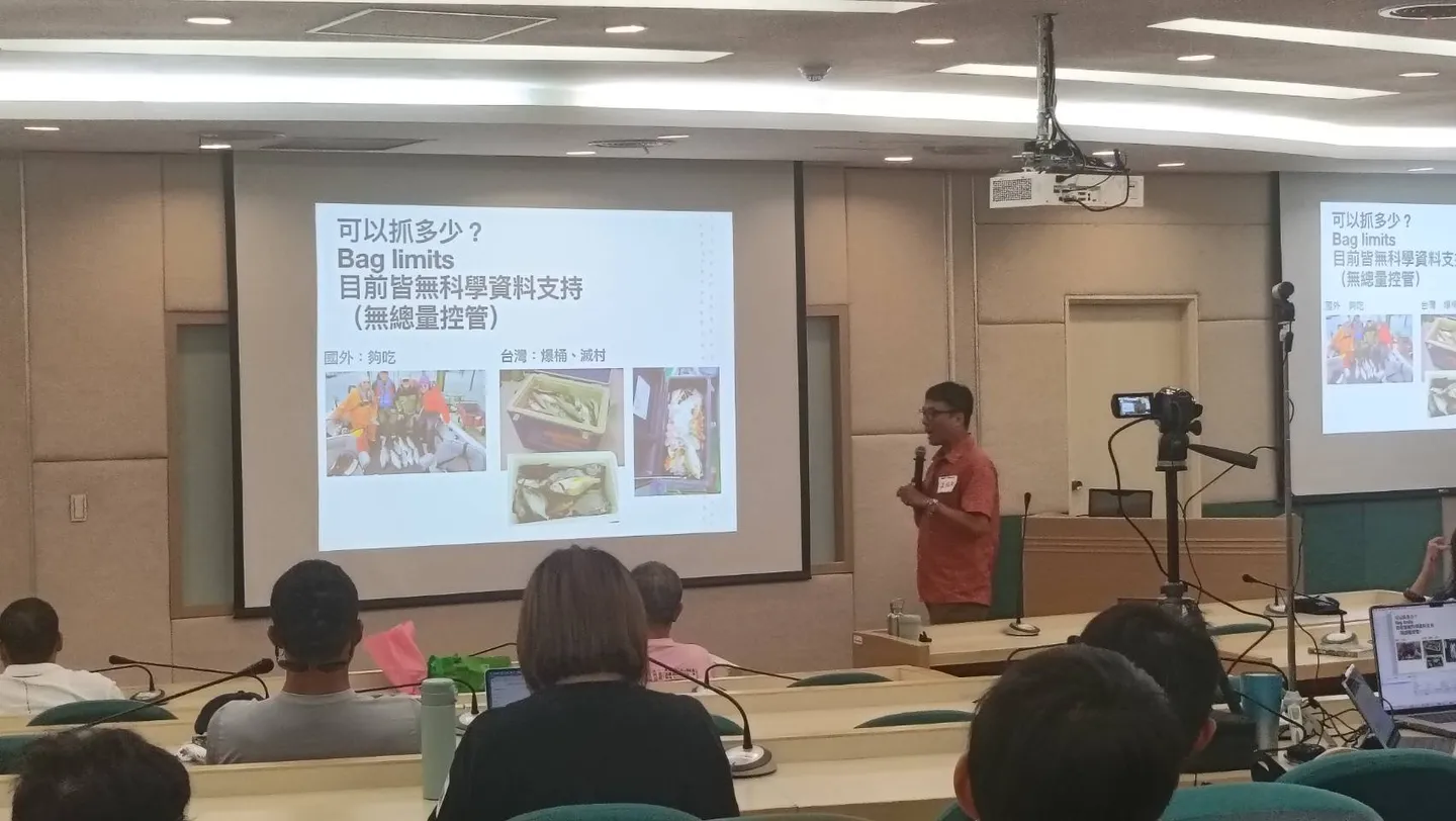 溫國彰教授站在投影幕旁演講，畫面上的簡報標題寫著「可以抓多少？Bag limits 目前皆無科學資料支持（無總量控管）」