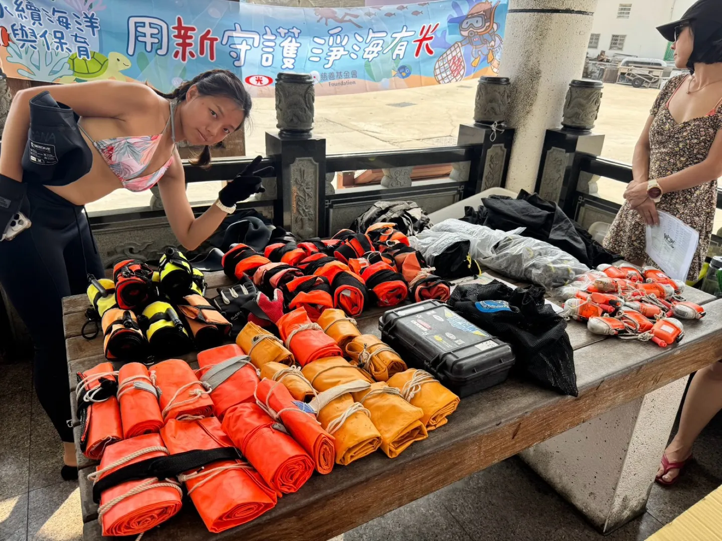 岸邊長桌上整齊排列著捲好的橘色與黃色浮力袋、捲軸與工作手套