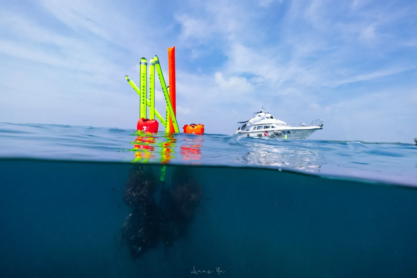 海面上三支立起的浮力袋標記著待運的漁網，水下可見成團的網具，遠方是接應的潛水船