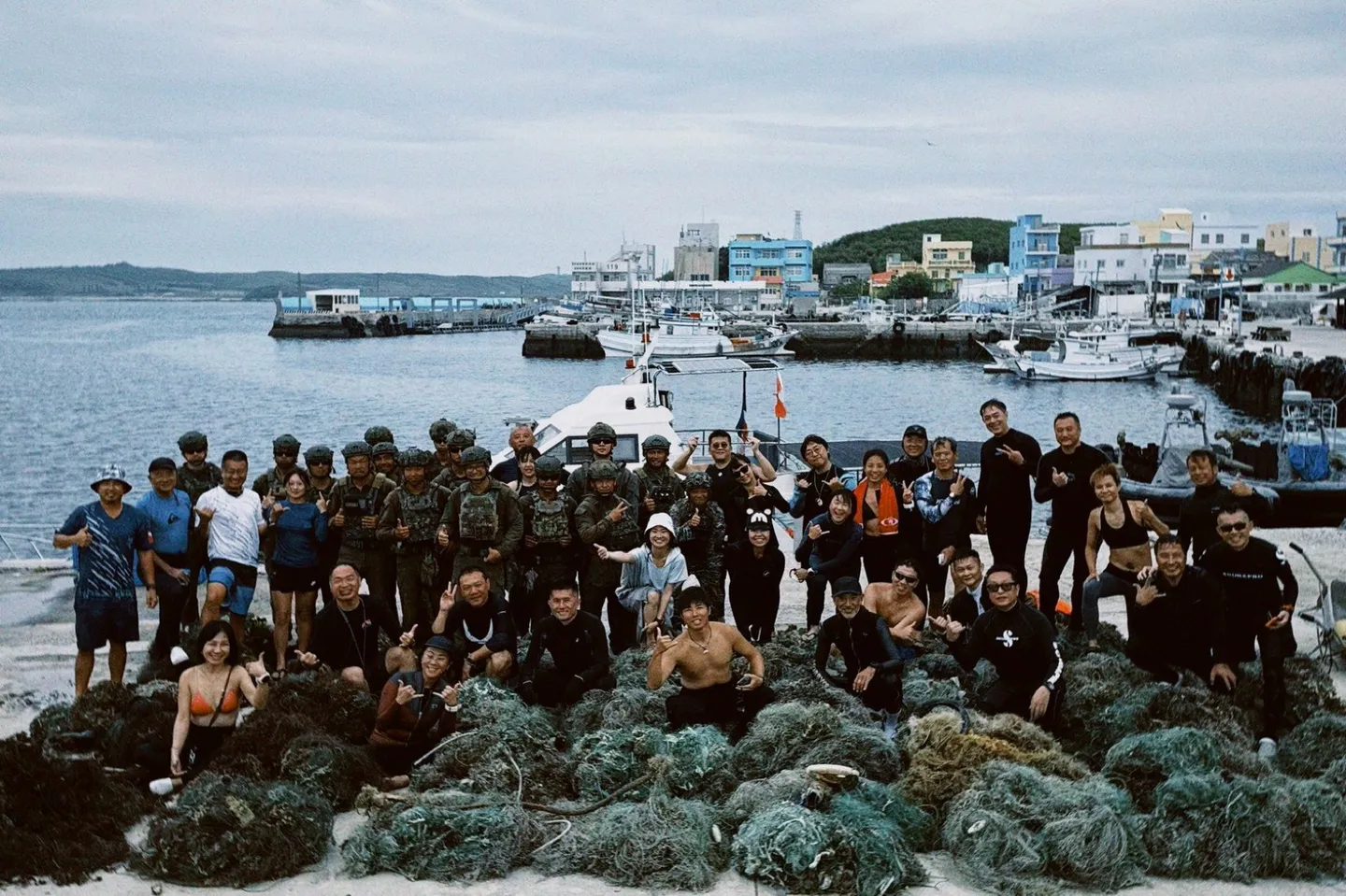 淨海結束後，潛水員與海龍部隊官兵在碼頭合影，眾人前方堆滿一團團剛清運上岸的廢棄漁網